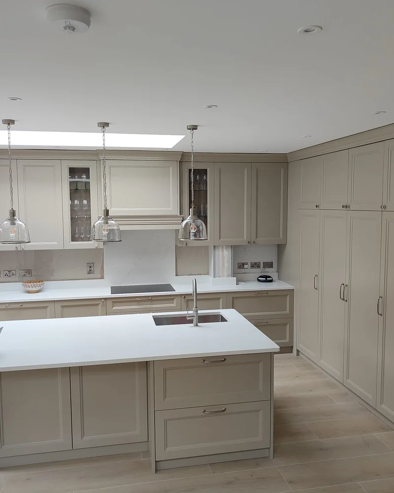 A bright classic painted fitted kitchen with a central island, display cabinets and full-height storage.