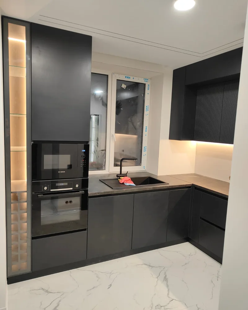 An alternative view of a dark handleless kitchen showing the built-in oven, sink and illuminated splashback.