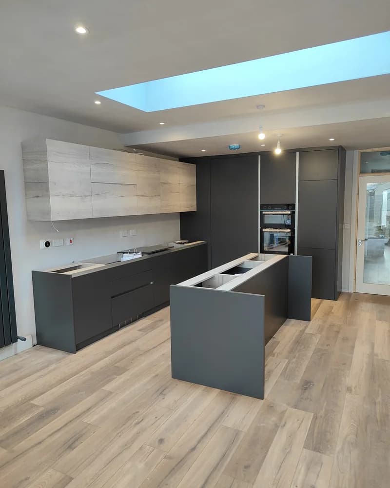 A contemporary graphite fitted kitchen with an island, timber flooring and a large roof light.
