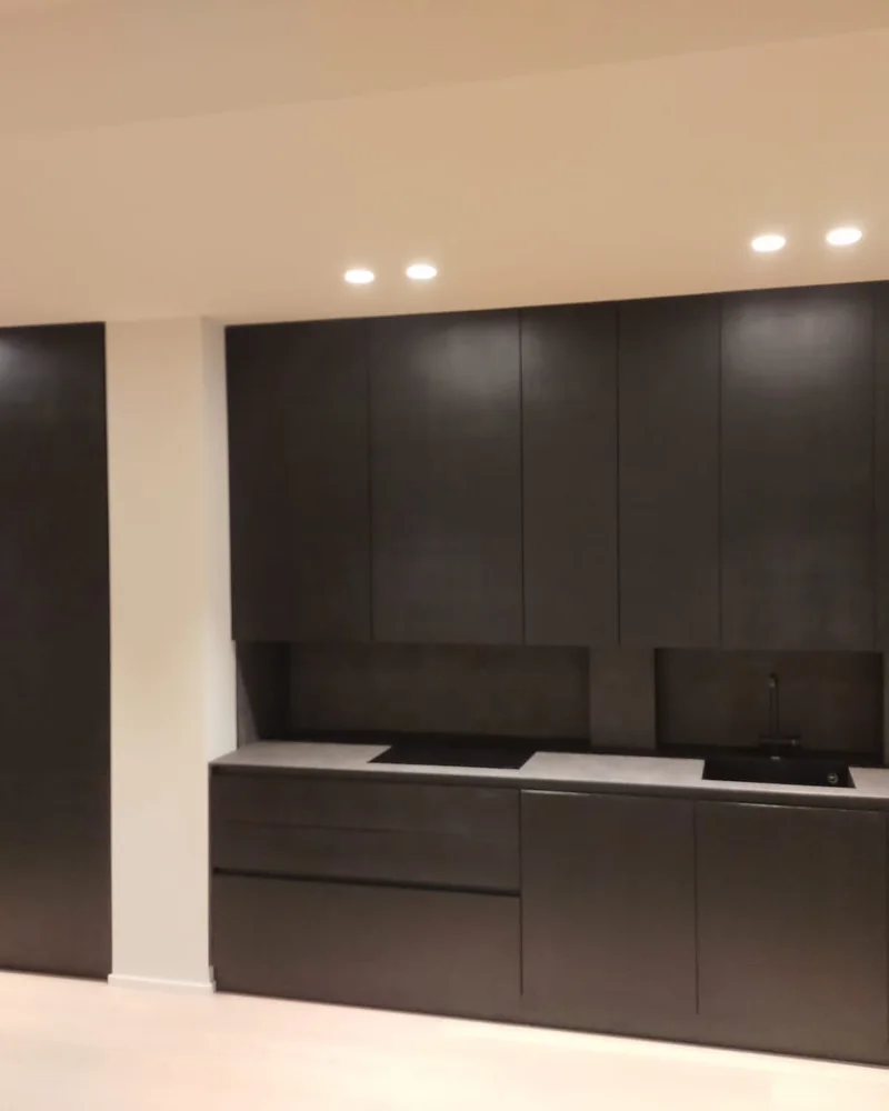 A minimalist dark fitted kitchen wall with integrated appliances and handleless storage.