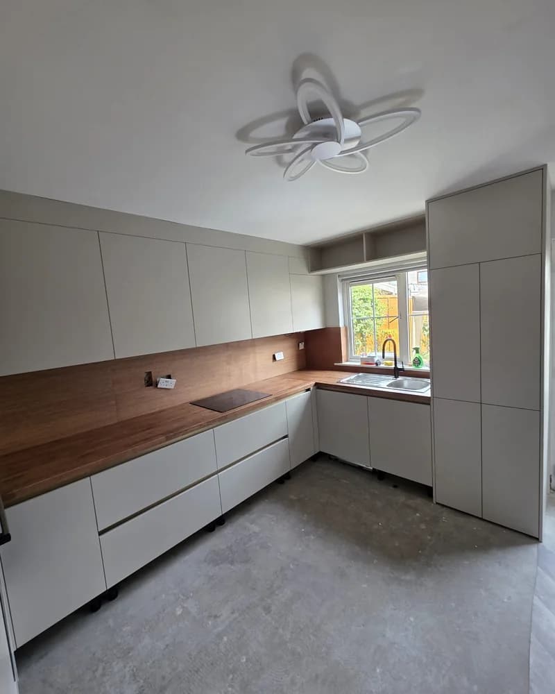 A light grey handleless corner kitchen with a warm timber worktop and tall fitted cabinetry.