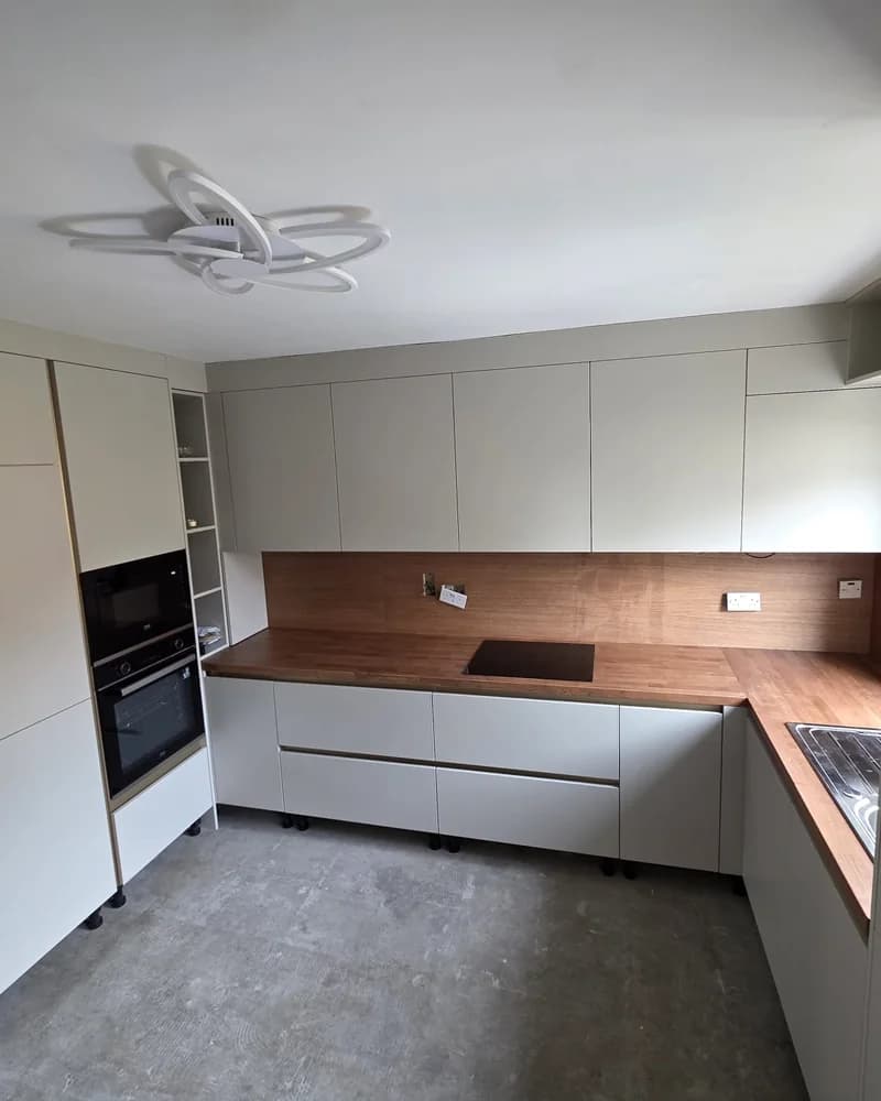 An alternative wide view of a light grey fitted kitchen with timber worktops and integrated ovens.