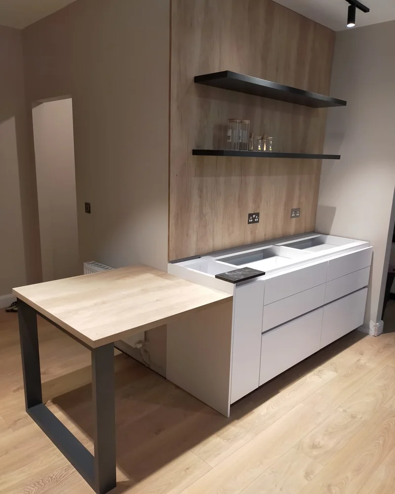 A neutral fitted kitchen with a timber island extension, open shelving and integrated storage.