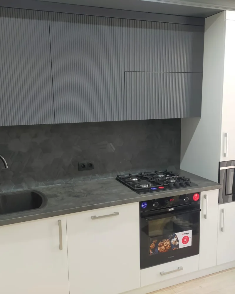 A compact two-tone fitted kitchen with pale base cabinets, grey wall cabinets and integrated appliances.