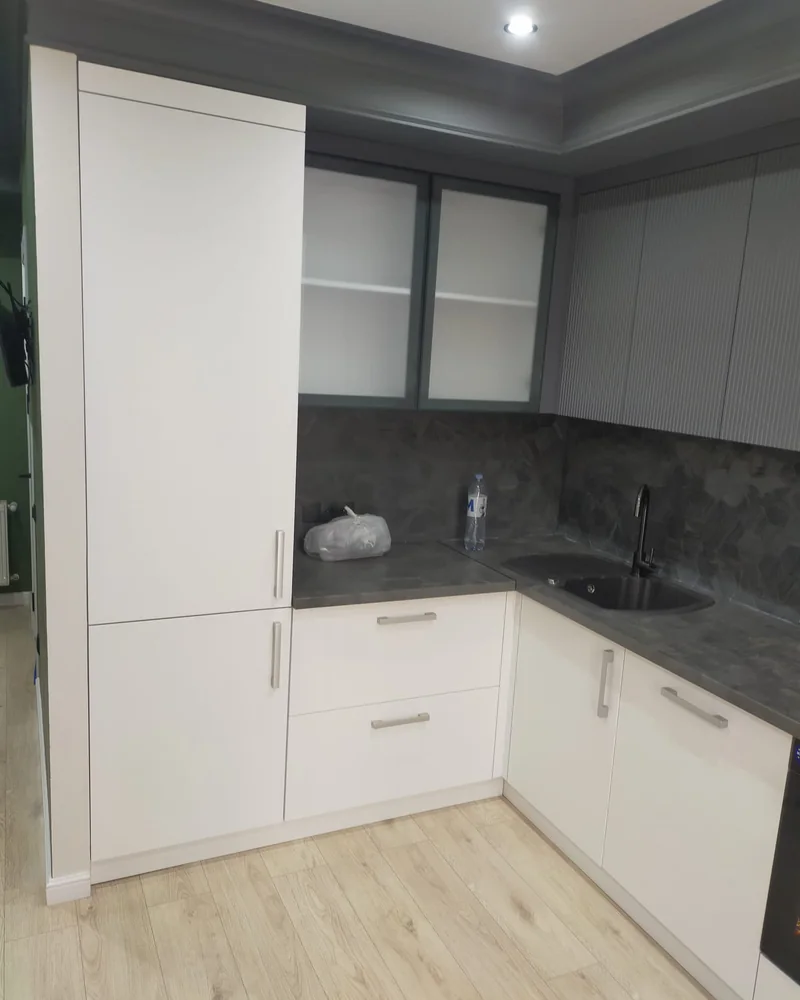 A closer view of a compact two-tone corner kitchen with glazed wall units and a dark worktop.