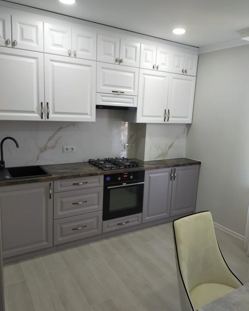 A traditional grey shaker-style fitted kitchen with detailed cabinetry and a marble-effect splashback.