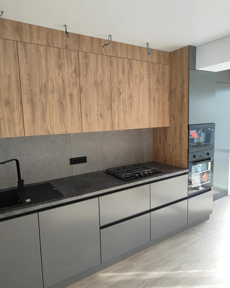 A contemporary fitted kitchen combining white handleless base units, wood wall cabinets and a dark worktop.