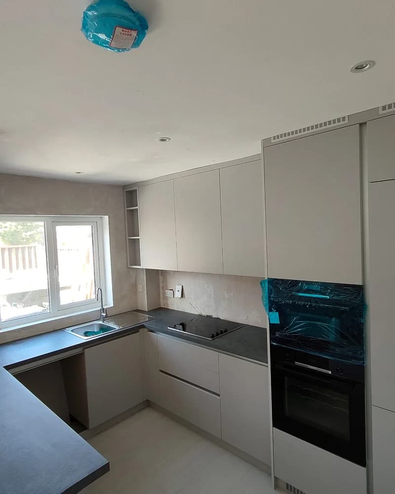 An alternative view of a light grey kitchen showing the peninsula, sink and tall fitted cabinets.