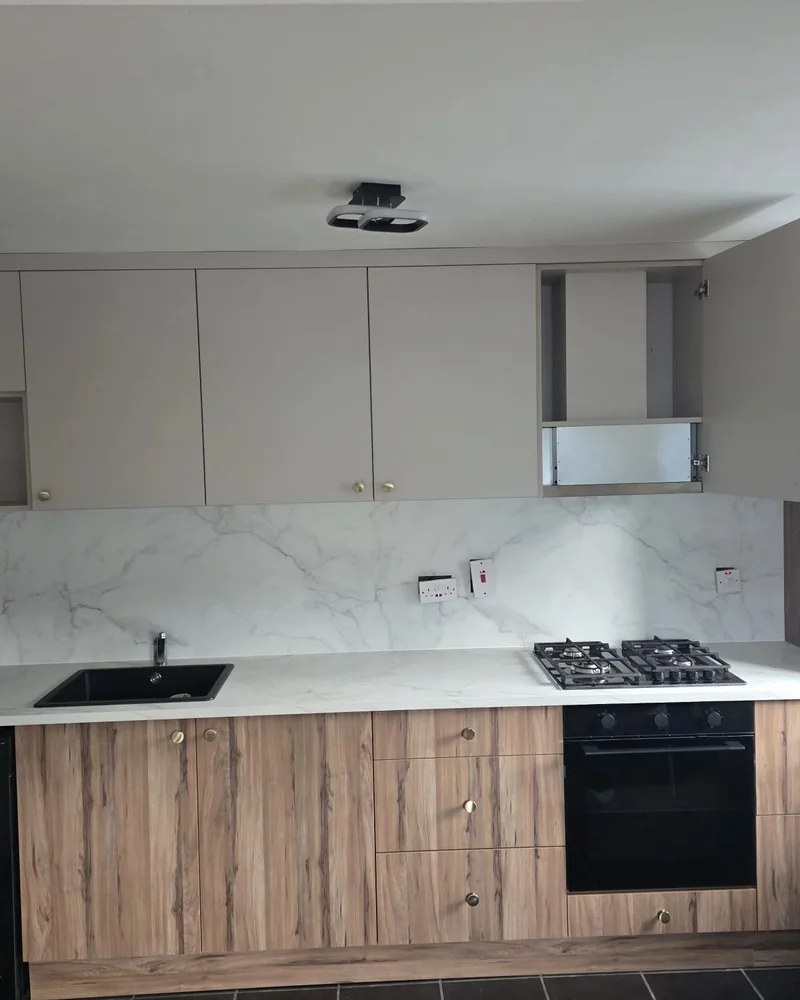 A compact fitted kitchen with wood-effect base cabinets, white wall units and integrated utility appliances.