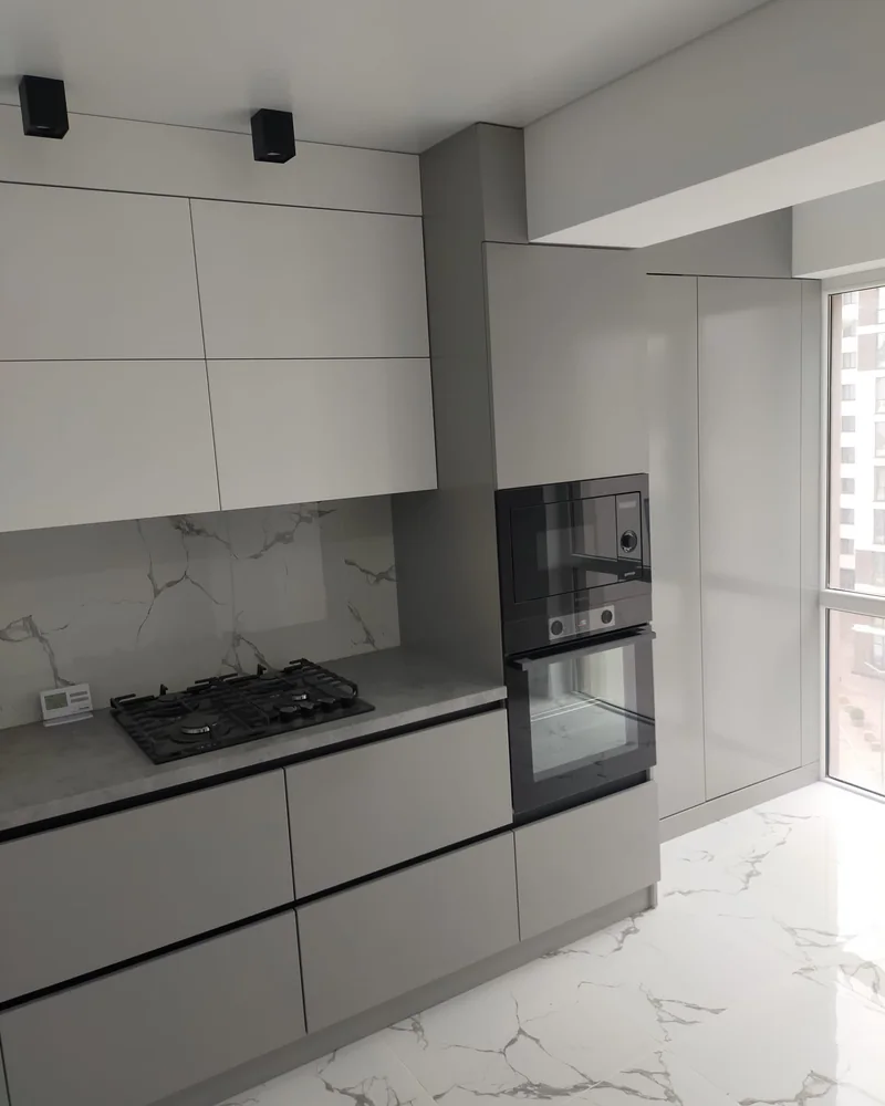 A matte grey fitted kitchen with integrated ovens, a black worktop and marble-effect splashback.