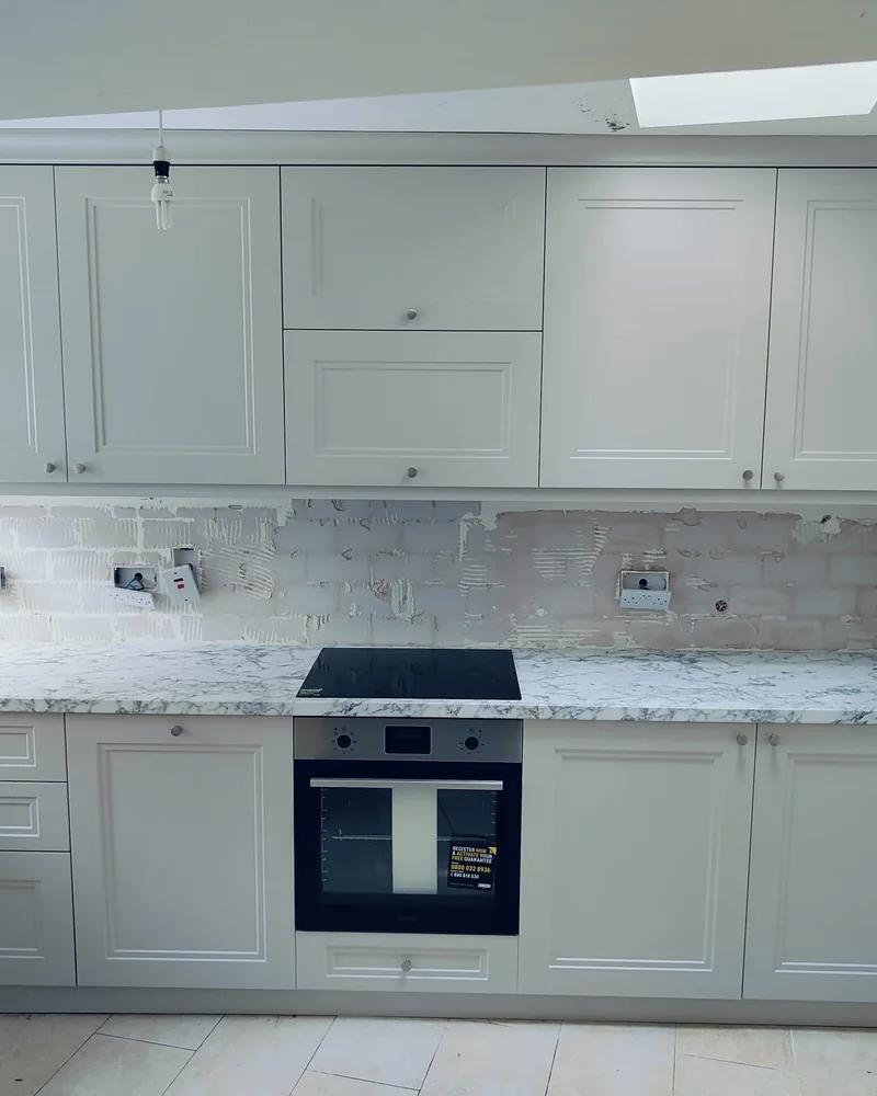 A bright white shaker fitted kitchen with an integrated oven and marble-effect worktops.