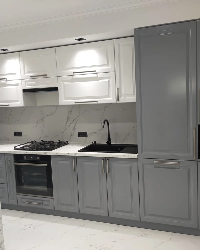 A grey framed fitted kitchen with glass display cabinets, integrated appliances and pale worktops.