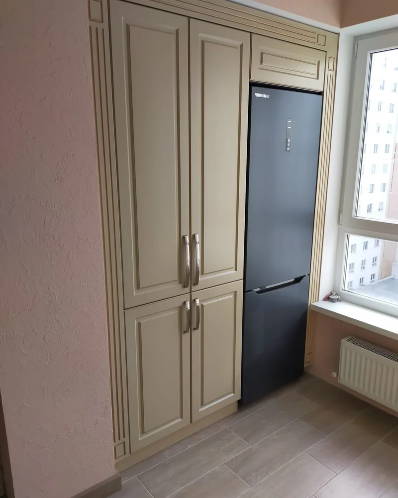 Classic tall fitted kitchen storage with detailed doors and an integrated refrigerator beside the window.