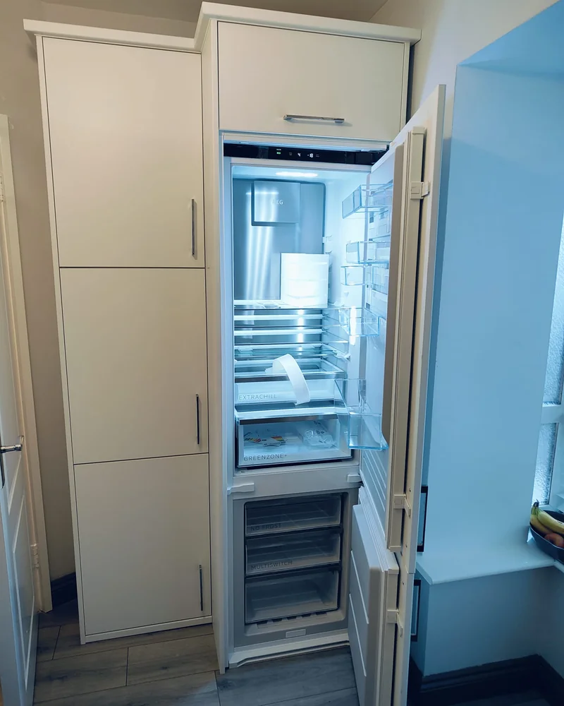 An open integrated refrigerator within a full-height fitted kitchen cabinet installation.