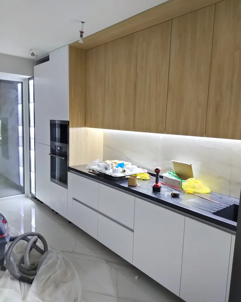 A modern white and oak fitted kitchen with integrated ovens and warm under-cabinet lighting.