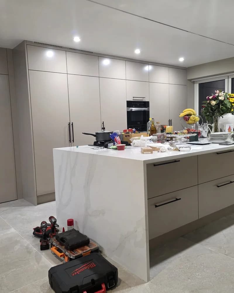 A premium neutral fitted kitchen with a large waterfall island, integrated appliances and full-height storage.