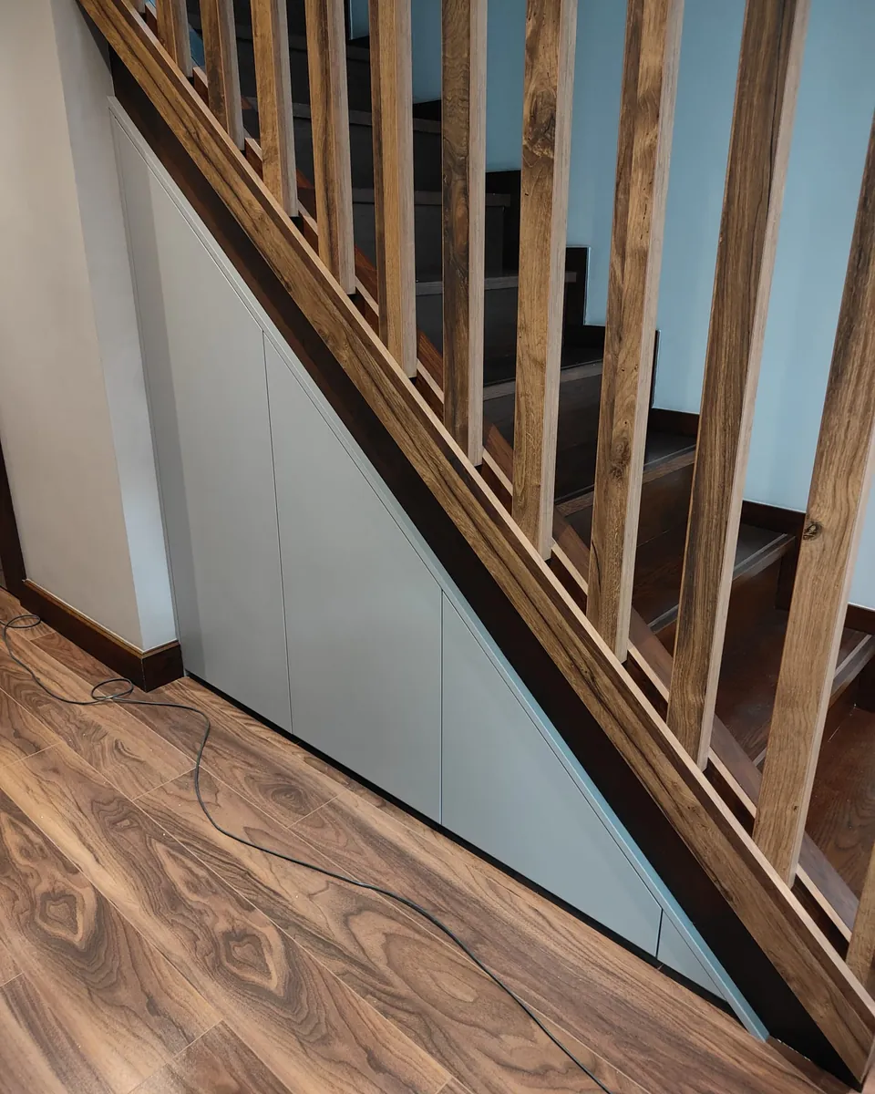 Custom grey under-stairs storage fitted beneath a timber staircase