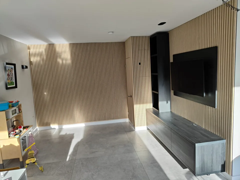 Wide view of a custom oak slat TV wall with concealed door and floating cabinet