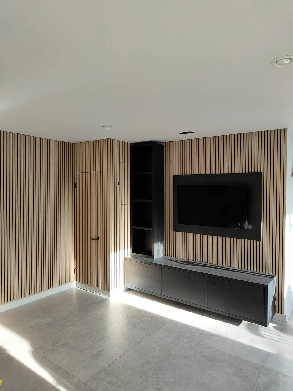 Front view of an oak slat TV media wall with a dark floating cabinet