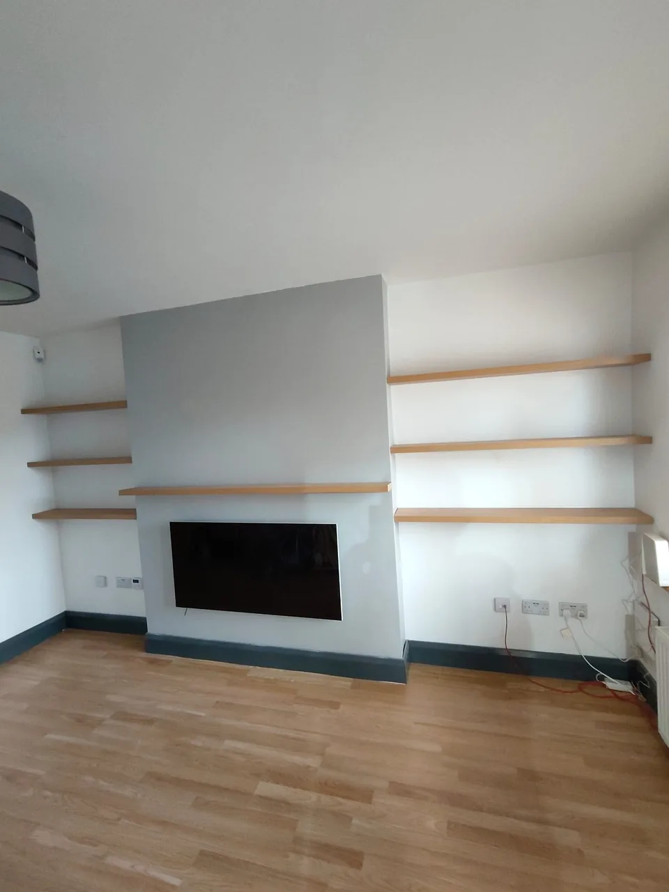 Completed grey fireplace media wall with timber display shelves and television space
