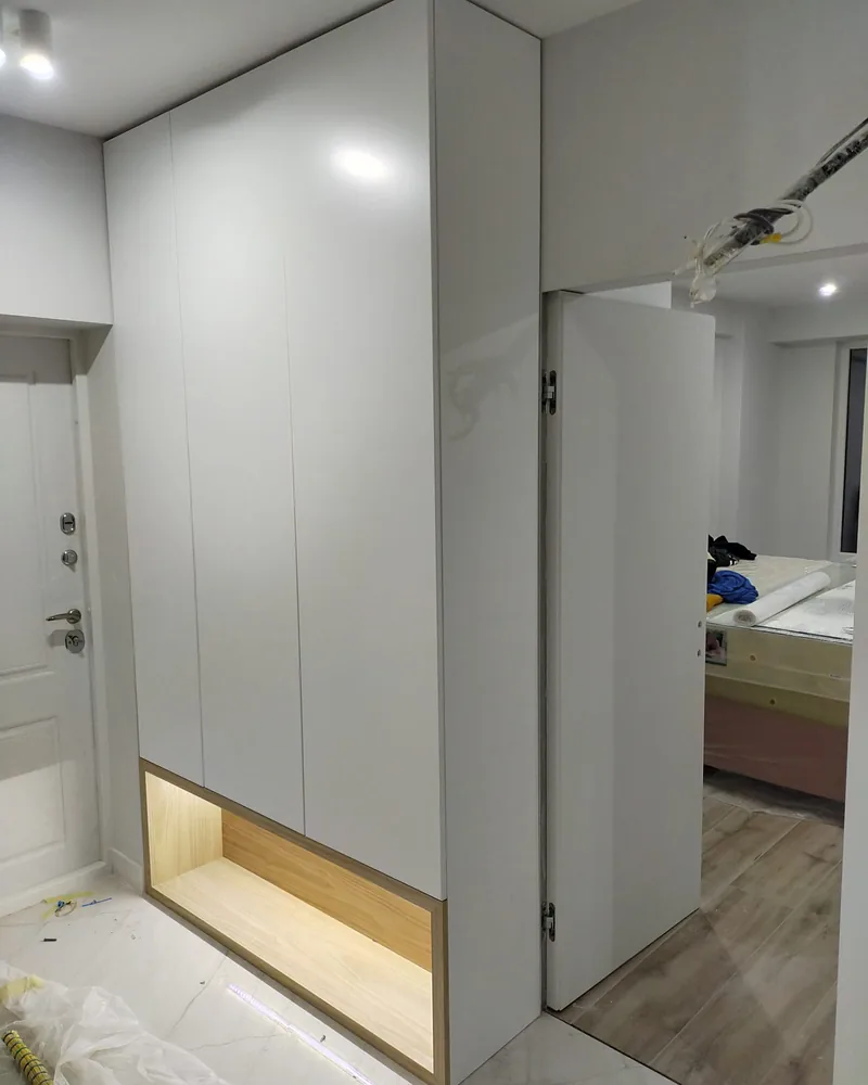 A light grey fitted hallway wardrobe with a full-height mirrored panel and illuminated open base detail.