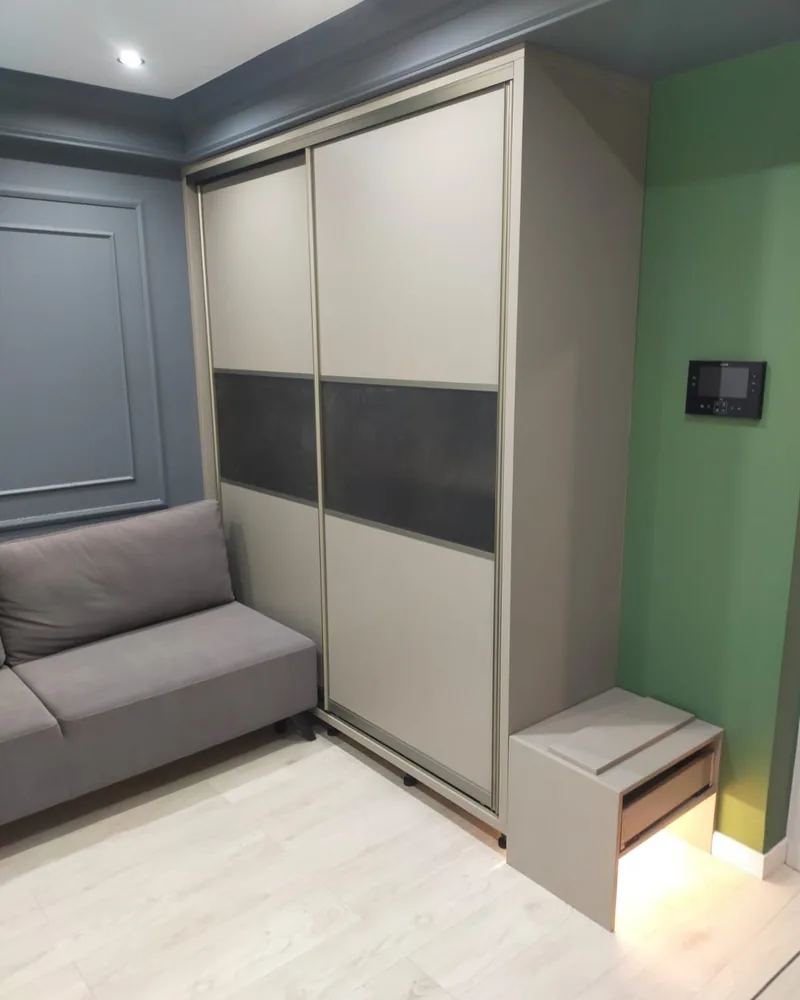 A grey sliding-door fitted wardrobe with dark inset panels and a matching compact bedside unit.