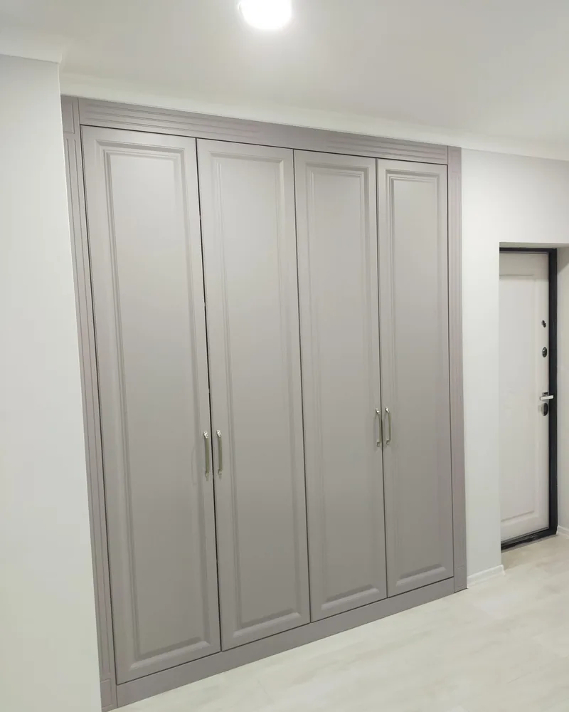 A classic grey four-door fitted wardrobe with framed panel doors and traditional handles.