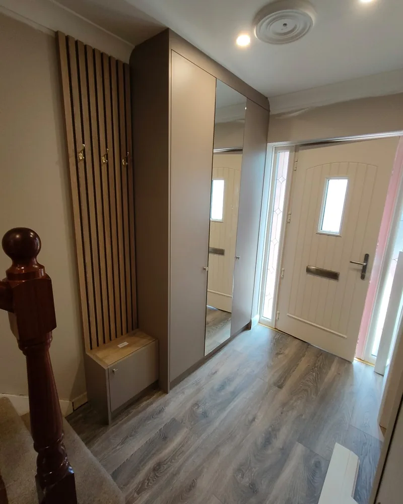A bespoke hallway storage installation with warm timber cabinetry, vertical slatted panelling and concealed lighting.