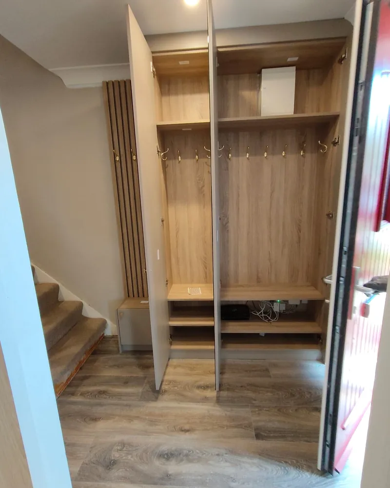 An open fitted wardrobe interior showing timber shelving, hanging rails and lower drawer storage.