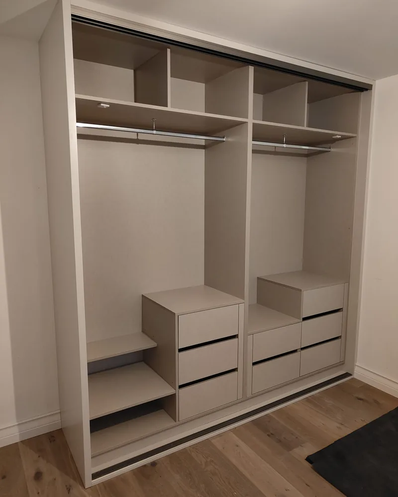 The interior of a fitted sliding wardrobe with shelves, hanging rails, drawers and open storage compartments.