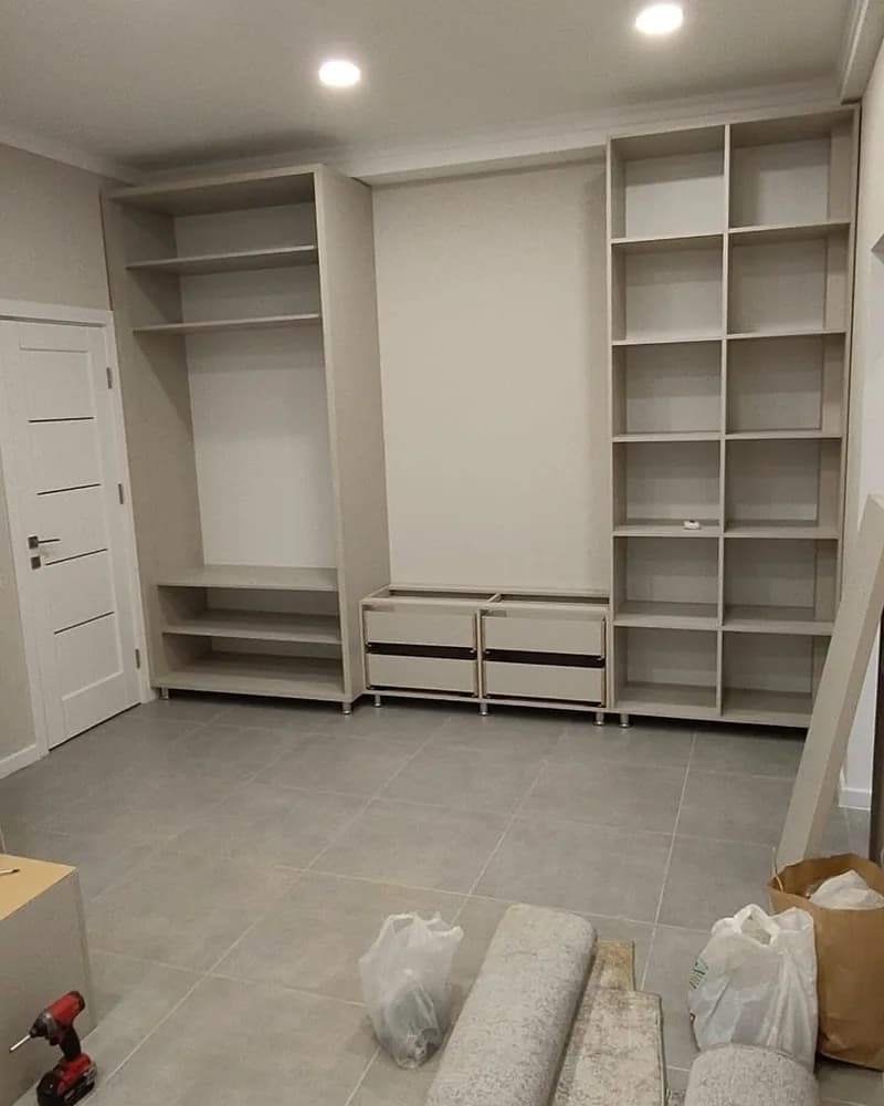 A full-wall open wardrobe installation with extensive shelving, hanging space and lower storage during fitting.