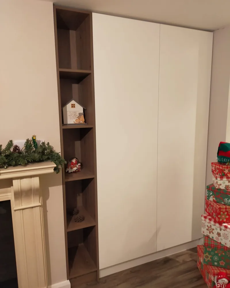A white fitted wardrobe beside a fireplace with integrated dark open shelving for display and storage.