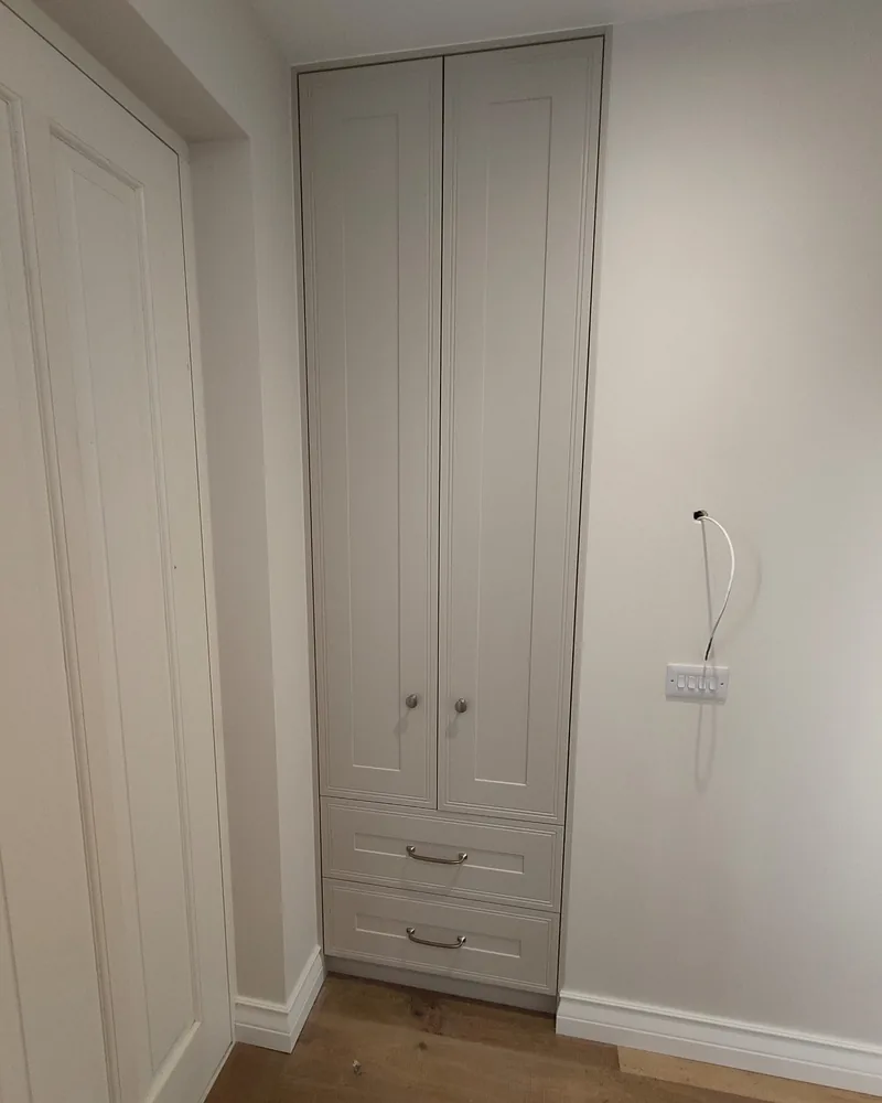 A narrow grey fitted wardrobe with panel doors, lower drawers and a ceiling-height finish.