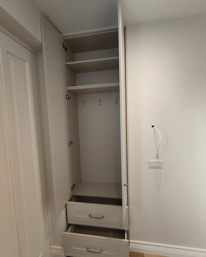 The open interior of a narrow fitted wardrobe with hanging rails, shelves, drawers and compact storage sections.
