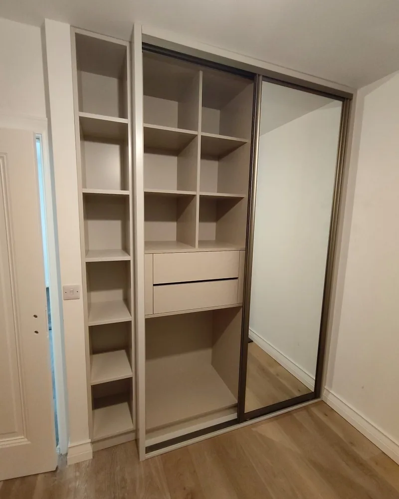 A fitted sliding wardrobe shown open with internal shelves, hanging rails and warm neutral finishes.