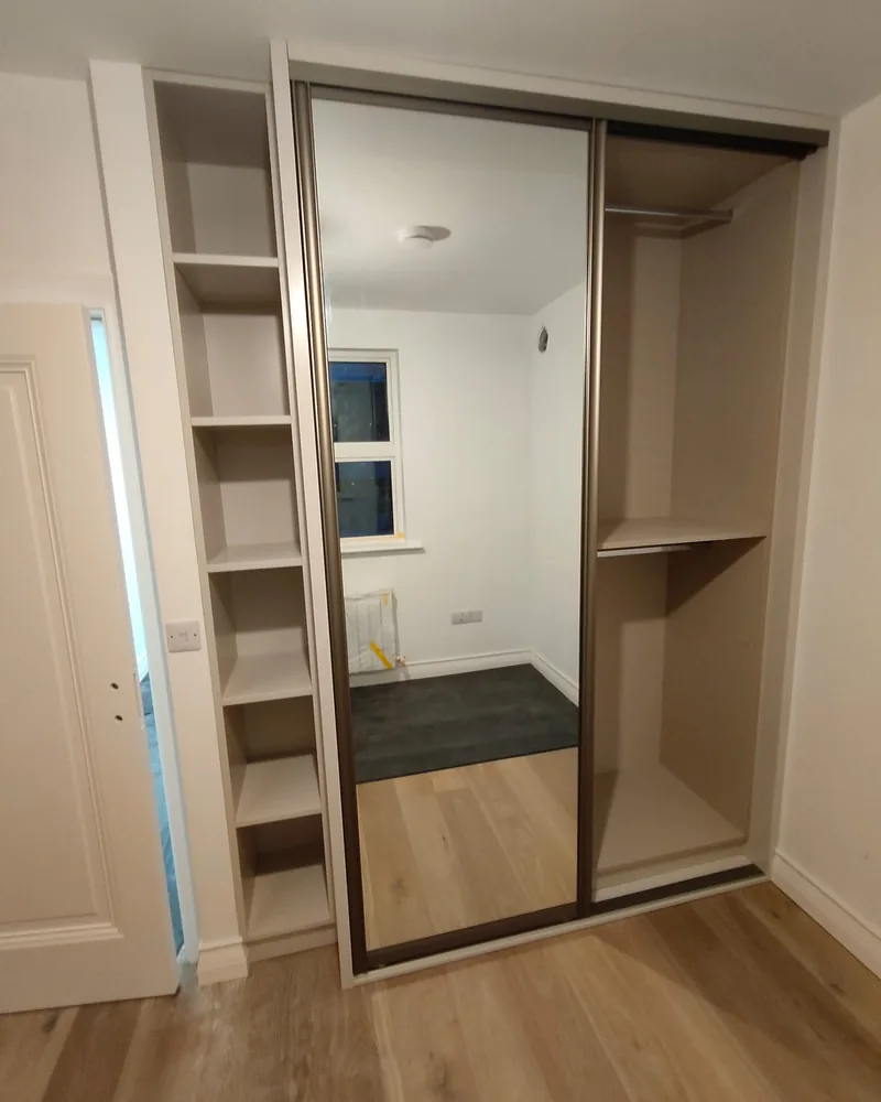 An open mirrored sliding wardrobe showing shelving and hanging space beside the reflective door panel.