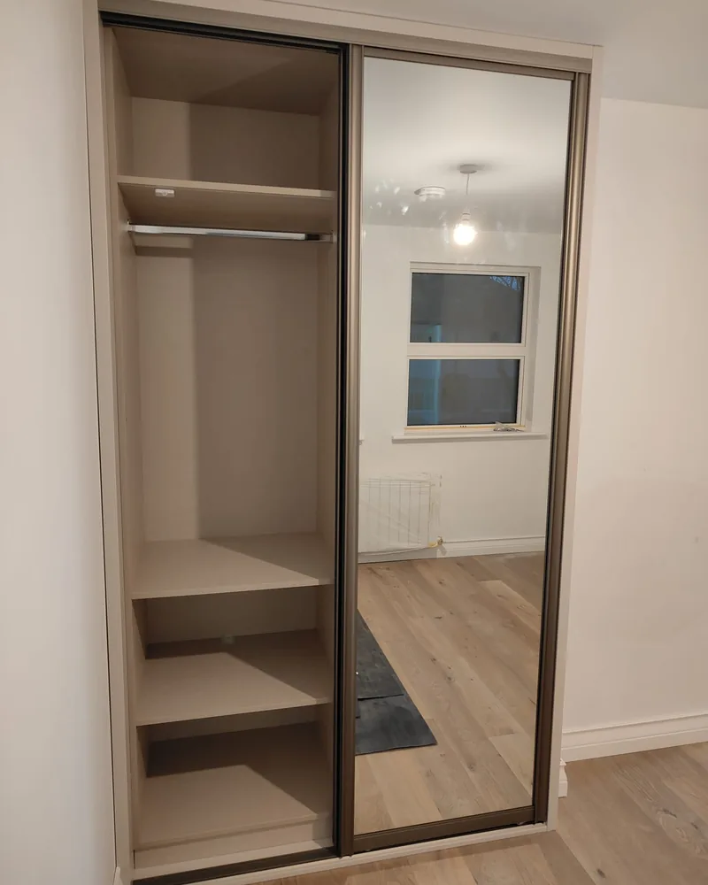 A close view of a mirrored sliding wardrobe interior with hanging rails and vertical shelving.