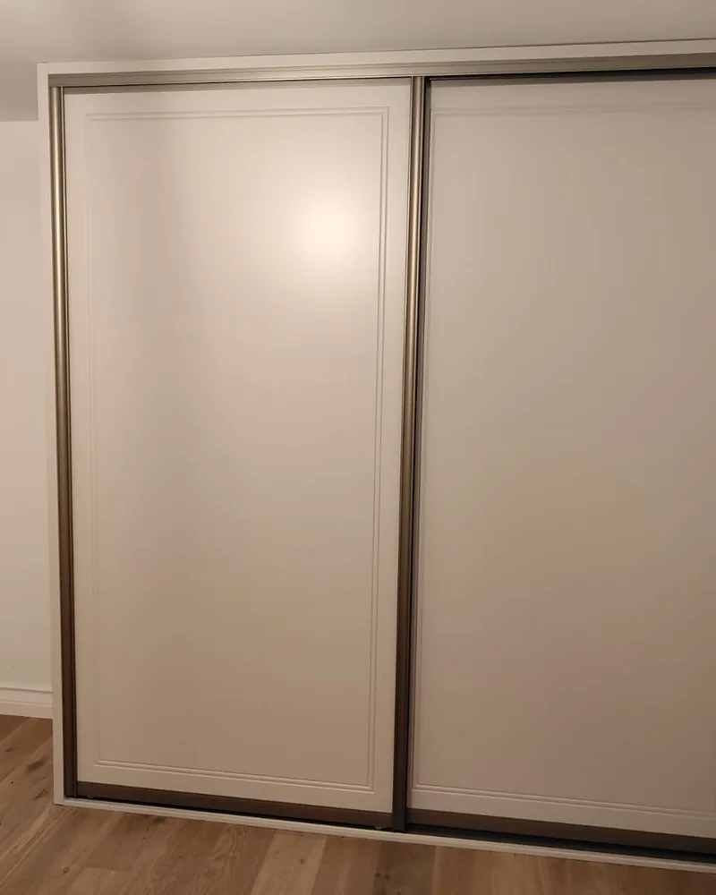 A neutral two-door sliding wardrobe with slim dark tracks fitted across a bedroom wall.