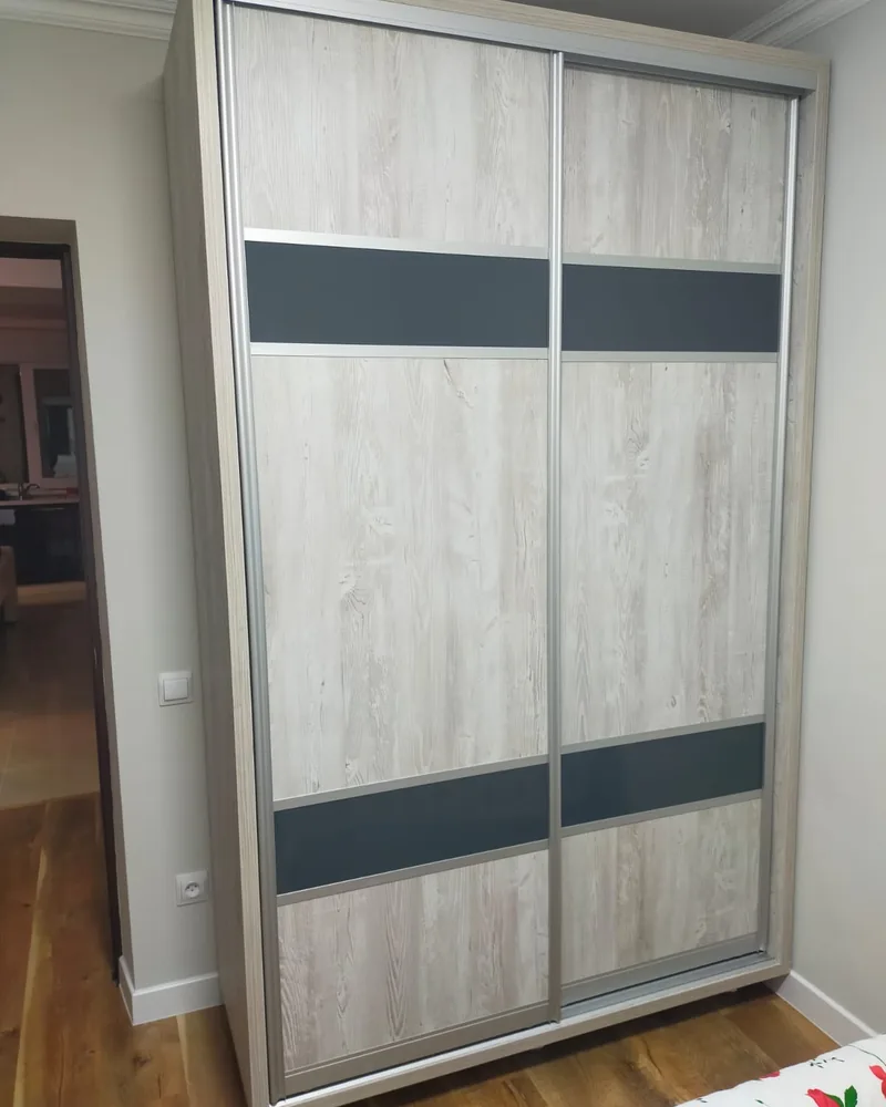 A light wood sliding wardrobe with dark horizontal feature bands and matching frame details.