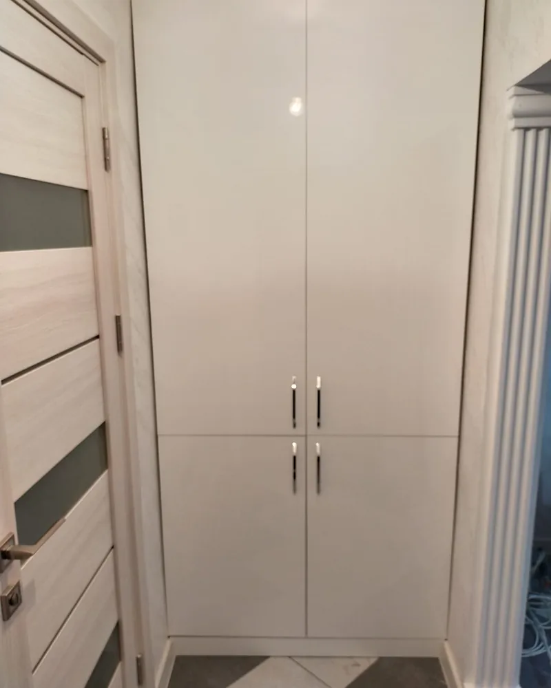 A white fitted hallway wardrobe with double panel doors and full-height cabinetry.
