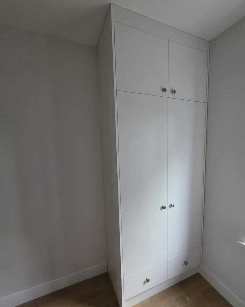 A simple white fitted wardrobe installed into a bedroom alcove with discreet handles and top infill.