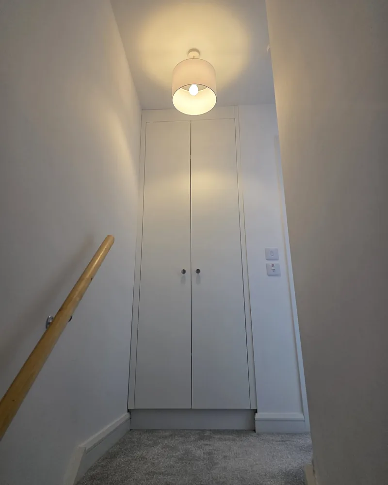 A tall white built-in cupboard fitted neatly at the top of a stairwell with ceiling-height doors.
