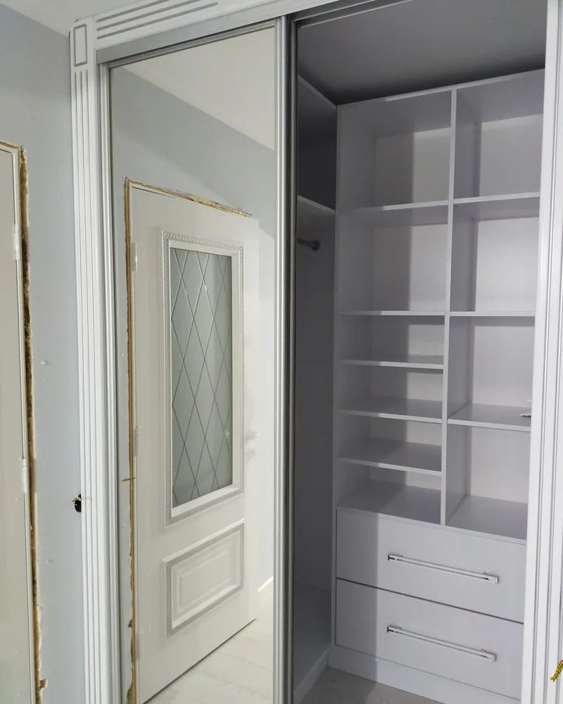 An open hallway wardrobe showing shelves, hanging space and a bank of integrated drawers.
